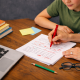 Parent helping a child revise a printed essay with handwritten corrections at a desk.