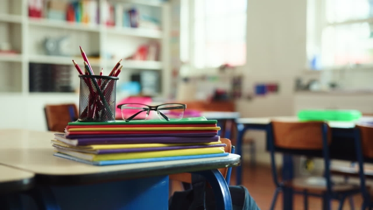 Student desk with pencil and standardized test booklet in soft natural light, empty classroom setting.