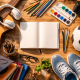 Flat lay of diverse hobbies including a guitar, soccer ball, art supplies, camera, and open notebook arranged on a wooden desk.