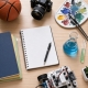 Flat lay of a desk with notebooks, camera, paint palette, violin, basketball, and science tools representing diverse high school electives.