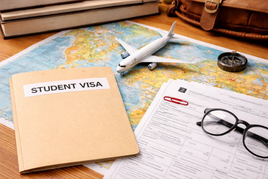 Student visa folder and I-20 paperwork on a world map with a model airplane, glasses, and travel accessories on a wooden desk