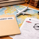 Student visa folder and I-20 paperwork on a world map with a model airplane, glasses, and travel accessories on a wooden desk