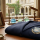 A scholarly wooden desk featuring a folded navy blue school blazer with a generic crest, surrounded by vintage books, laboratory flasks, a globe, and a compass, set against a blurred courtyard window.