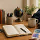 Cozy study desk with an open notebook, globe, plants, colorful books, and art supplies in warm natural light, symbolizing creativity and diversity.