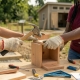 Students collaborating outdoors on a woodworking service project, using a hammer and drill to build a wooden box.