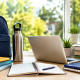 Sunlit study desk with backpack, books, laptop, and school supplies by a window, suggesting summer learning.