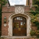 An ivy-covered brick college building with large wooden double doors, featuring an architectural stone crest above the entrance.