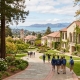 An elevated view of a scenic Bay Area private school campus with ivy-covered buildings, redwood trees, and students walking on paths, overlooking a distant view of the Golden Gate Bridge and the bay.