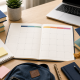 Top-down view of a tidy desk with an open monthly planner, laptop, notebooks, and study supplies in soft natural light.