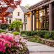Modern private school campus courtyard with landscaped garden, blooming flowers, and contemporary academic buildings in soft daylight.