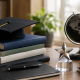 Graduation cap on stacked books with a globe and trophy on a desk, symbolizing academic success and future achievements.